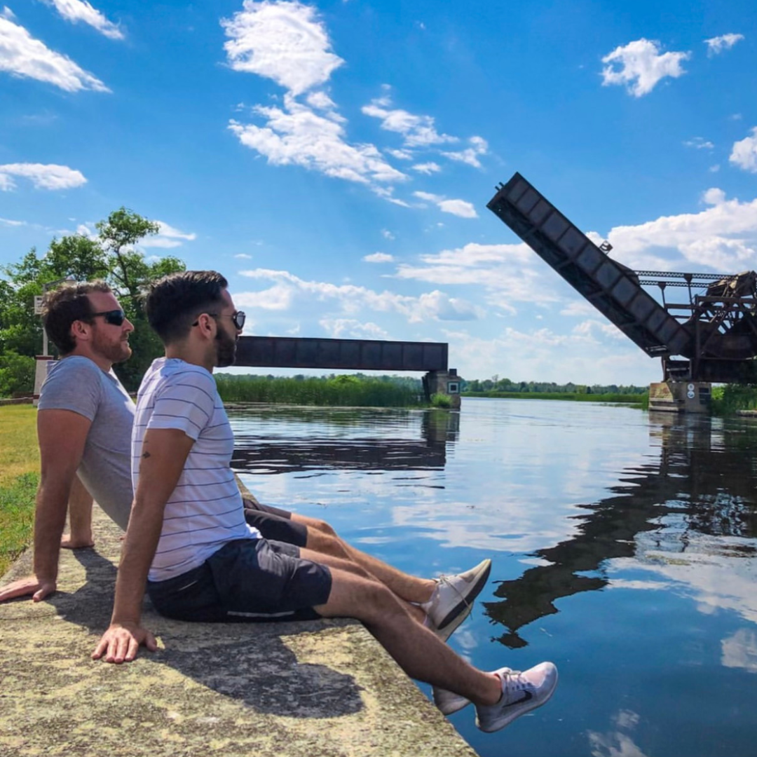 Two men relax on the wall of the Rideau Canal basin with the iconic Bascule Bridge in the background.