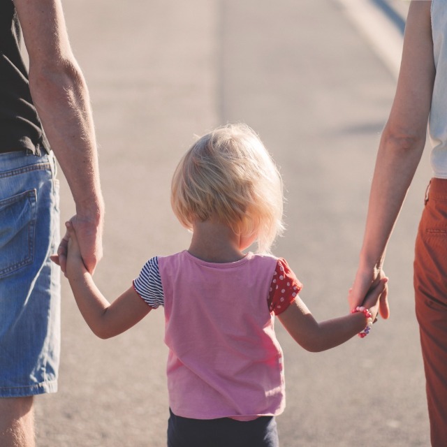 A child wearing a pink shirt holds the hands of two adults.