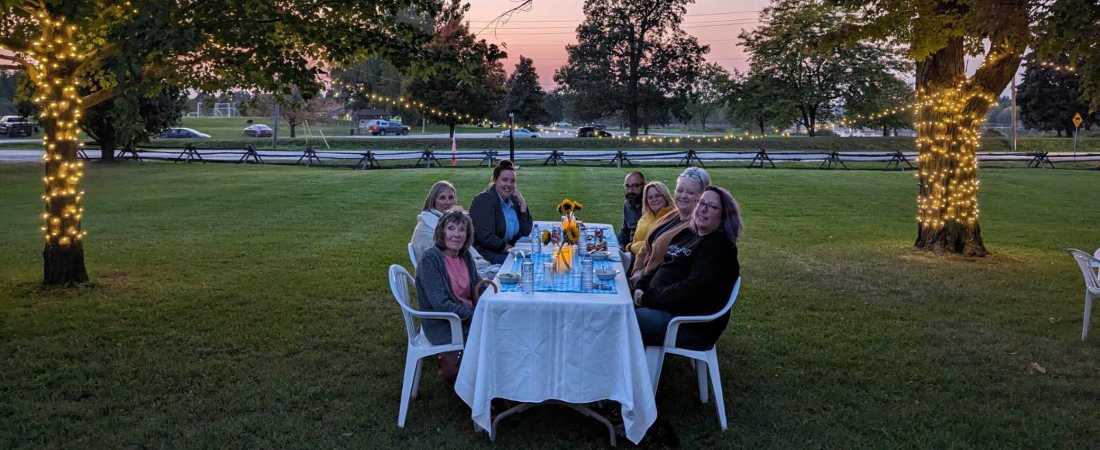 group of people at a table, eating outside in the evening