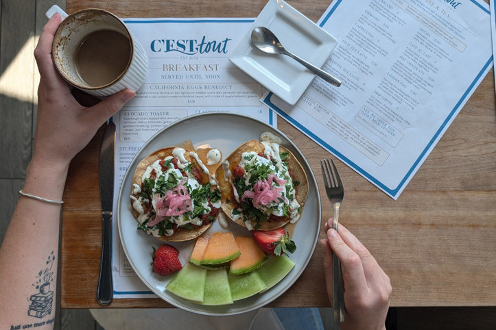 A guest at Cest Tout Bakery sits at a table with a coffee and breakfast bagel.